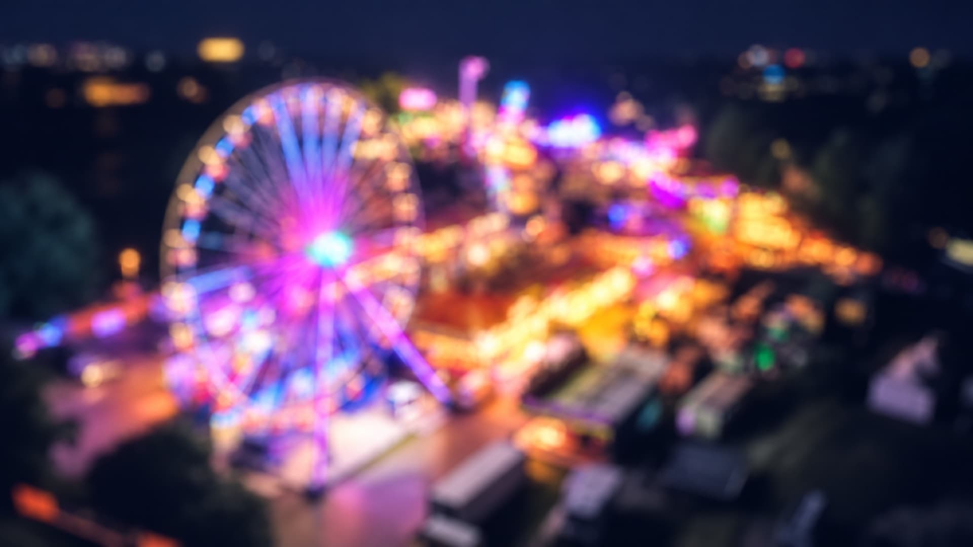 Beleuchtetes Riesenrad und Fahrgeschäfte auf einem Kirmesplatz bei Nacht